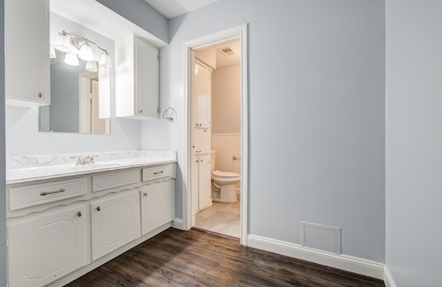 bathroom with toilet, wood finished floors, vanity, visible vents, and baseboards