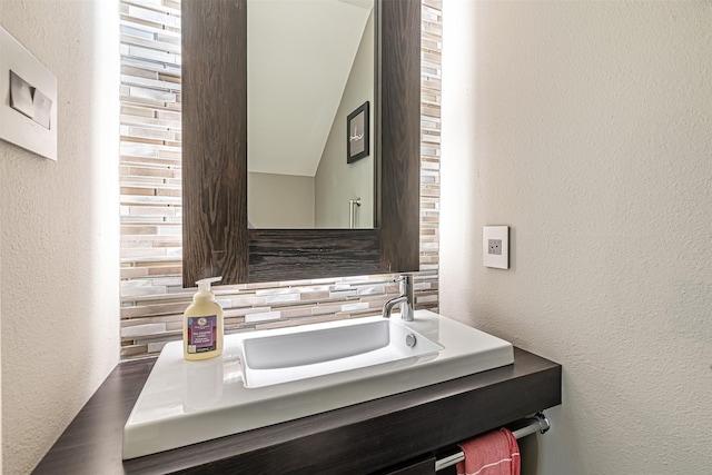 bathroom with a textured wall, a sink, and decorative backsplash