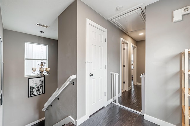 hallway with dark wood-style flooring, visible vents, attic access, an upstairs landing, and baseboards