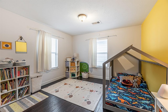 bedroom with visible vents, a textured ceiling, baseboards, and wood finished floors