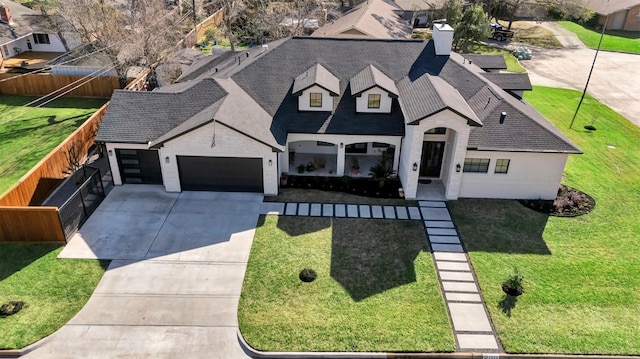 french country home featuring fence, concrete driveway, a front yard, a shingled roof, and an attached garage