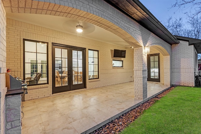 entrance to property featuring brick siding, a patio area, french doors, and a yard