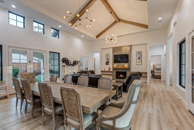 dining space featuring french doors, a large fireplace, a chandelier, and light wood finished floors