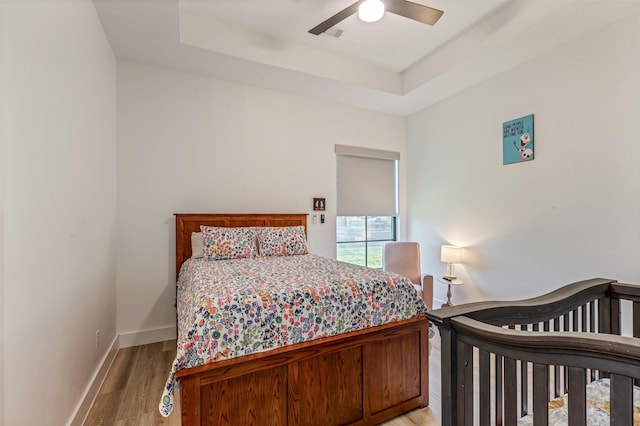 bedroom with a tray ceiling, baseboards, light wood-style floors, and ceiling fan