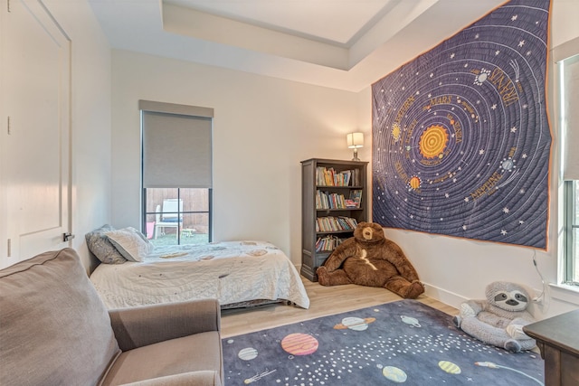 bedroom with a tray ceiling, multiple windows, and wood finished floors