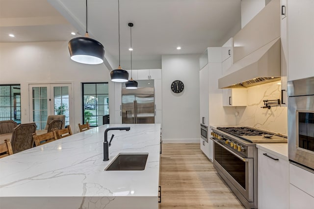 kitchen with light wood-type flooring, decorative backsplash, white cabinets, high end appliances, and a sink