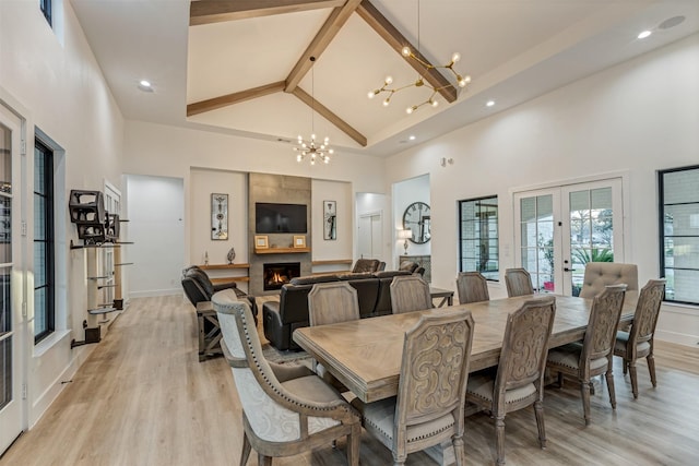 dining room with a large fireplace, a chandelier, french doors, light wood-style floors, and high vaulted ceiling