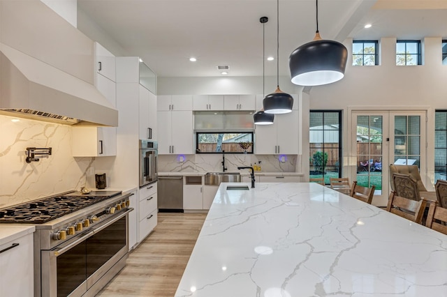 kitchen featuring light stone countertops, premium range hood, light wood-style flooring, appliances with stainless steel finishes, and white cabinetry