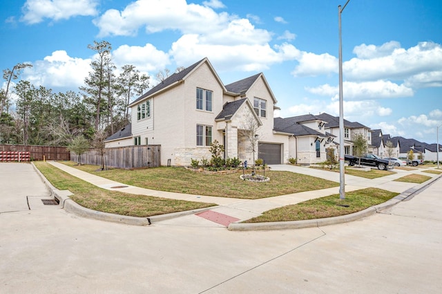 view of front facade with concrete driveway, an attached garage, fence, a residential view, and stone siding