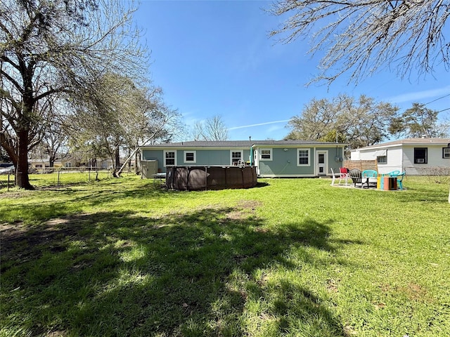 rear view of property with fence, an outdoor pool, and a yard