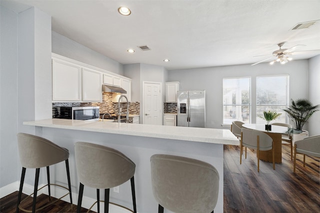 kitchen featuring visible vents, under cabinet range hood, tasteful backsplash, appliances with stainless steel finishes, and a peninsula