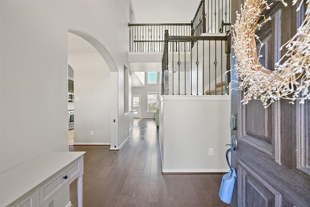 foyer entrance featuring arched walkways, stairs, baseboards, and wood finished floors