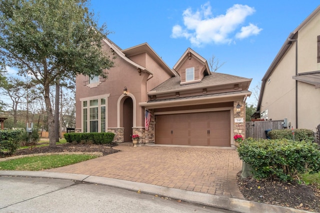 view of front of home featuring stone siding, fence, decorative driveway, and stucco siding