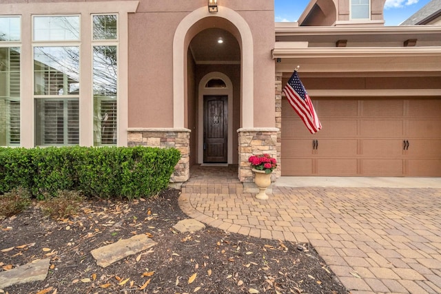 entrance to property with a garage, stone siding, decorative driveway, and stucco siding