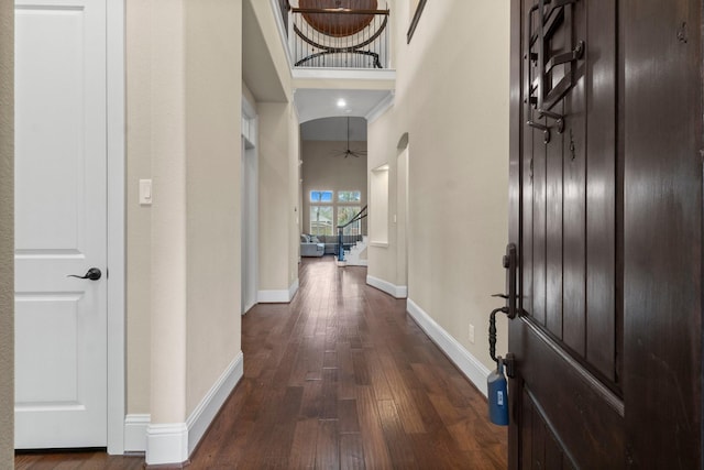 foyer entrance featuring baseboards, dark wood finished floors, arched walkways, a towering ceiling, and stairway