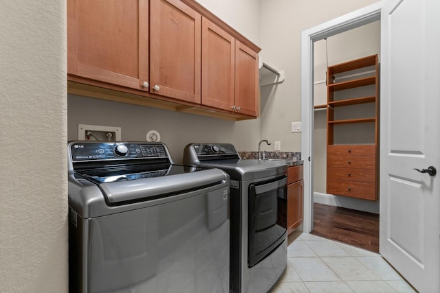 laundry area with washing machine and dryer, cabinet space, a sink, and light tile patterned floors