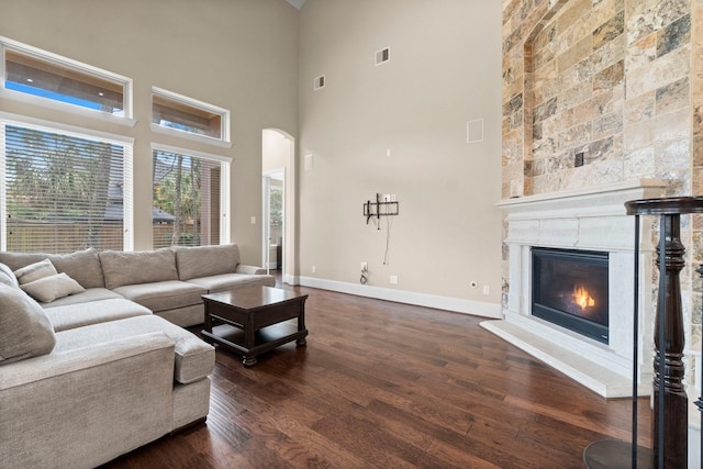 living area featuring arched walkways, dark wood-style flooring, a fireplace, visible vents, and baseboards