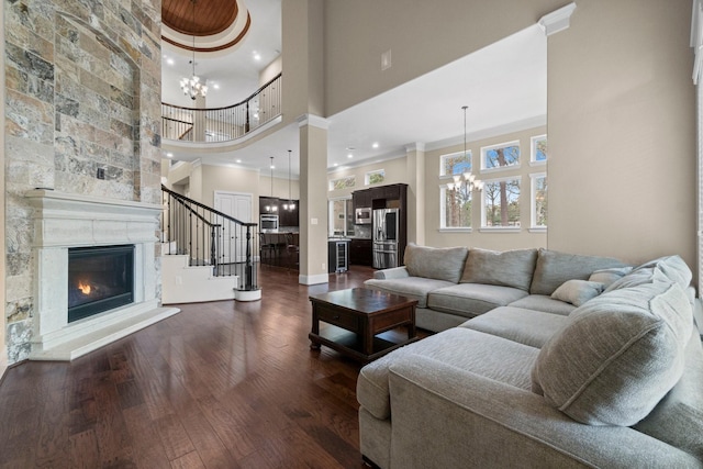 living room with dark wood-style floors, a fireplace, a notable chandelier, crown molding, and stairway