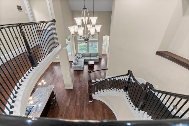 stairs with baseboards, arched walkways, wood finished floors, an inviting chandelier, and a high ceiling