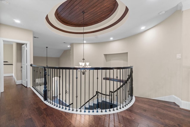 corridor with baseboards, wood-type flooring, an upstairs landing, and a notable chandelier