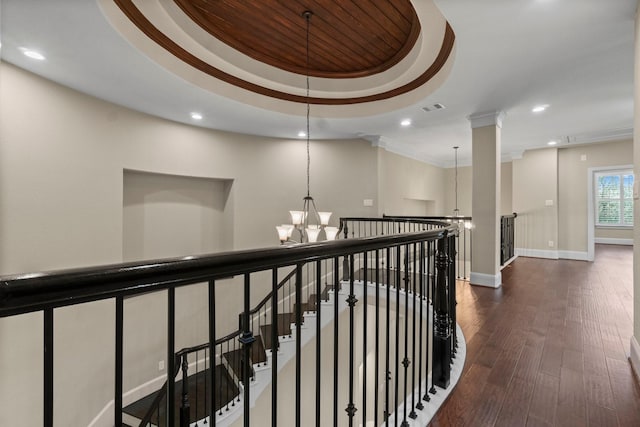 hall with dark wood-style floors, a tray ceiling, a notable chandelier, visible vents, and an upstairs landing