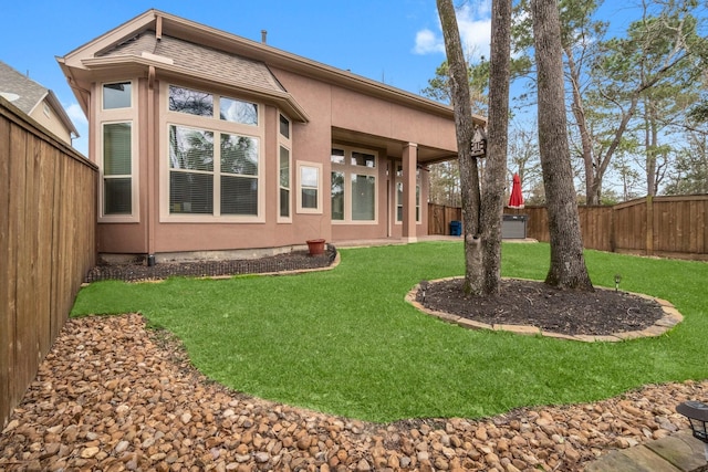 rear view of property with a yard, a fenced backyard, and stucco siding