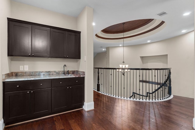 interior space featuring dark wood-style flooring, a raised ceiling, an inviting chandelier, a sink, and dark brown cabinets