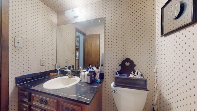 half bath with toilet, wallpapered walls, and vanity