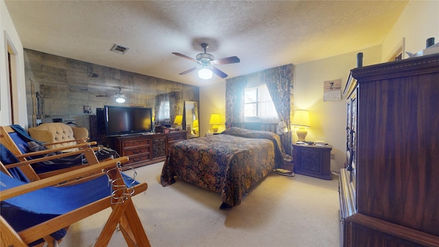 bedroom with a textured ceiling, an accent wall, visible vents, and light colored carpet