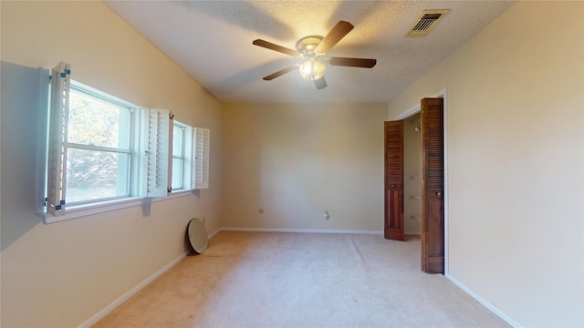 spare room with ceiling fan, a textured ceiling, light colored carpet, visible vents, and baseboards