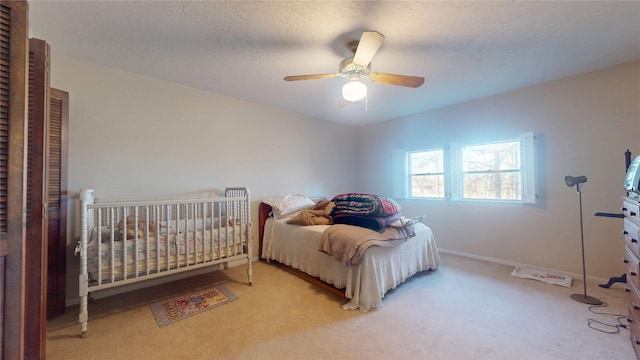 bedroom featuring light carpet, ceiling fan, baseboards, and a textured ceiling