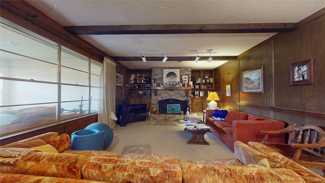 carpeted living area featuring beamed ceiling, rail lighting, a textured ceiling, wood walls, and a fireplace