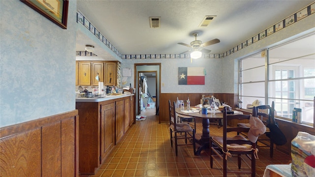 tiled dining area with ceiling fan, a textured ceiling, wainscoting, and visible vents