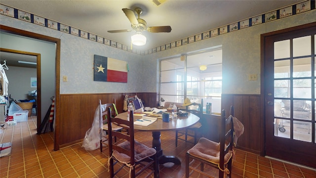 dining room featuring ceiling fan, wainscoting, and wooden walls