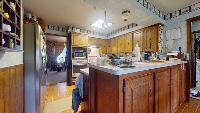 kitchen with wallpapered walls, stainless steel appliances, light countertops, and wainscoting