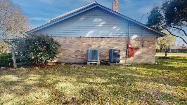 view of side of property featuring brick siding, a yard, a chimney, central AC unit, and fence