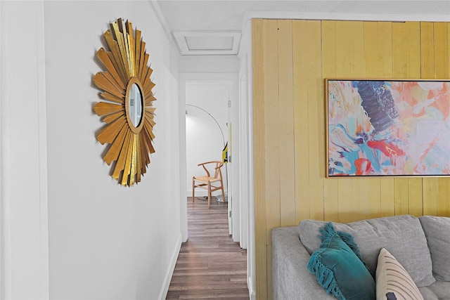 corridor featuring attic access, wooden walls, and wood finished floors