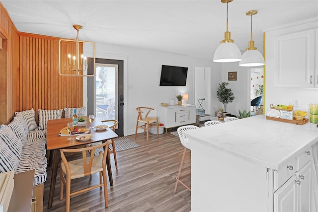 kitchen featuring white cabinets, a peninsula, light wood-type flooring, pendant lighting, and a notable chandelier