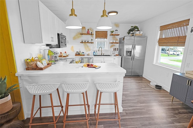 kitchen with a peninsula, a sink, appliances with stainless steel finishes, open shelves, and dark wood finished floors