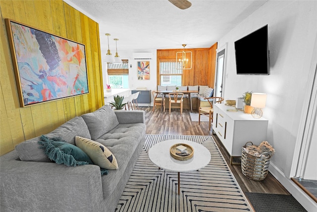 living area with wood finished floors, an inviting chandelier, a textured ceiling, an AC wall unit, and wood walls