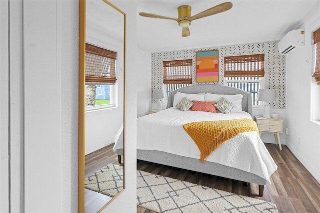 bedroom featuring a ceiling fan, a wall unit AC, baseboards, and wood finished floors