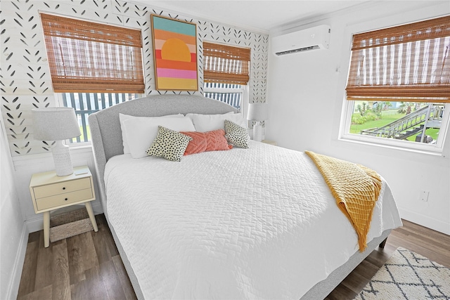 bedroom with a wall unit AC, baseboards, and wood finished floors