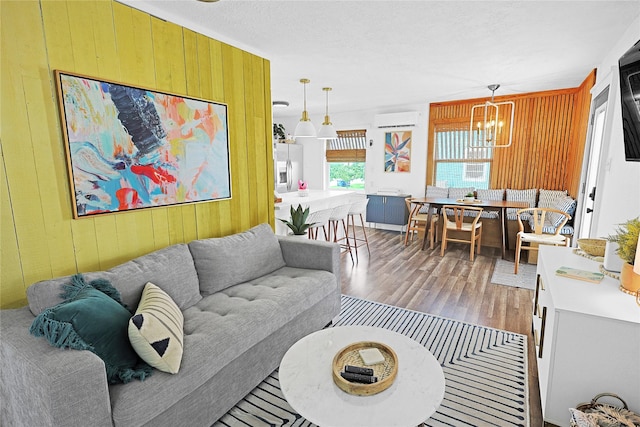 living area featuring wood walls, an inviting chandelier, wood finished floors, and a wall mounted AC