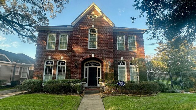 view of front of house featuring brick siding, a front lawn, and fence