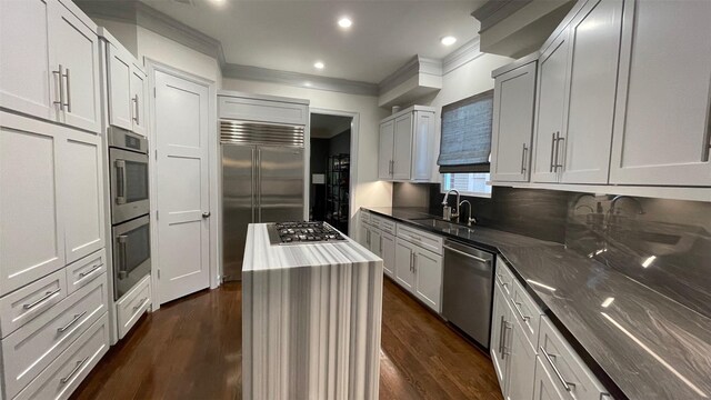 kitchen with stainless steel appliances, dark wood-style flooring, a sink, ornamental molding, and a center island