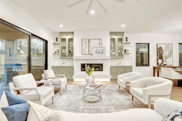 living area featuring light wood-type flooring, recessed lighting, ceiling fan, and a high end fireplace