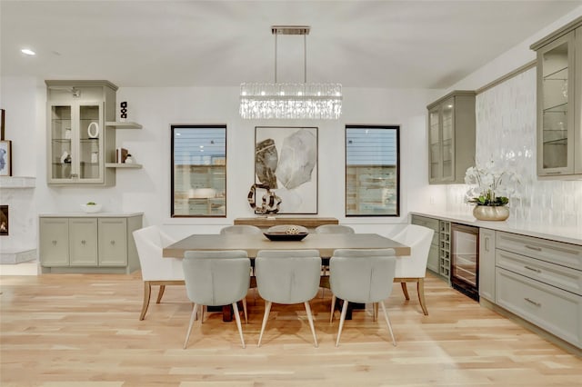 dining room with light wood-style floors, beverage cooler, a chandelier, and a premium fireplace