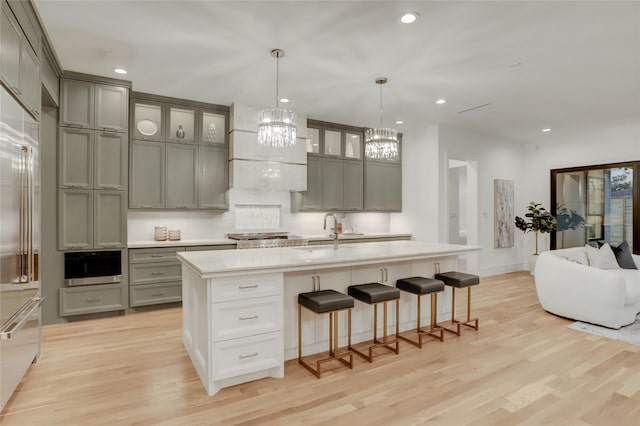 kitchen with light wood-type flooring, stainless steel built in fridge, a kitchen breakfast bar, and gray cabinetry