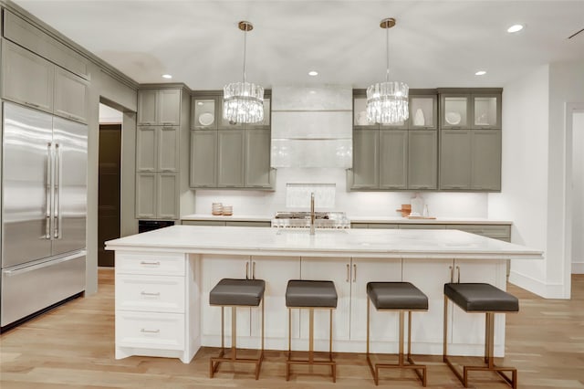 kitchen featuring built in fridge, light countertops, light wood-type flooring, wall chimney exhaust hood, and a kitchen bar