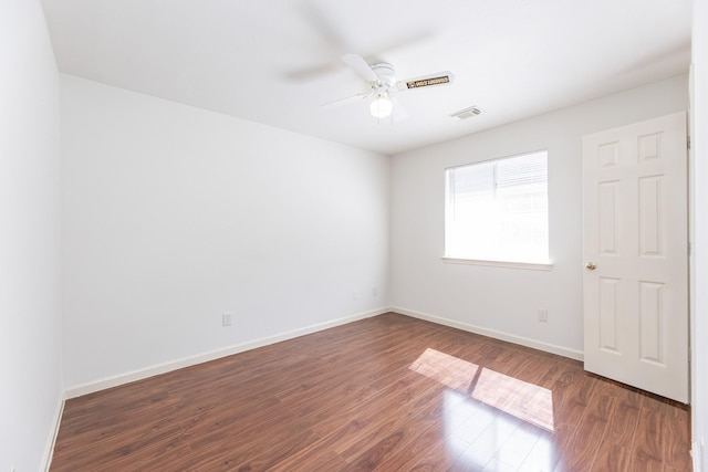 spare room with a ceiling fan, visible vents, baseboards, and wood finished floors